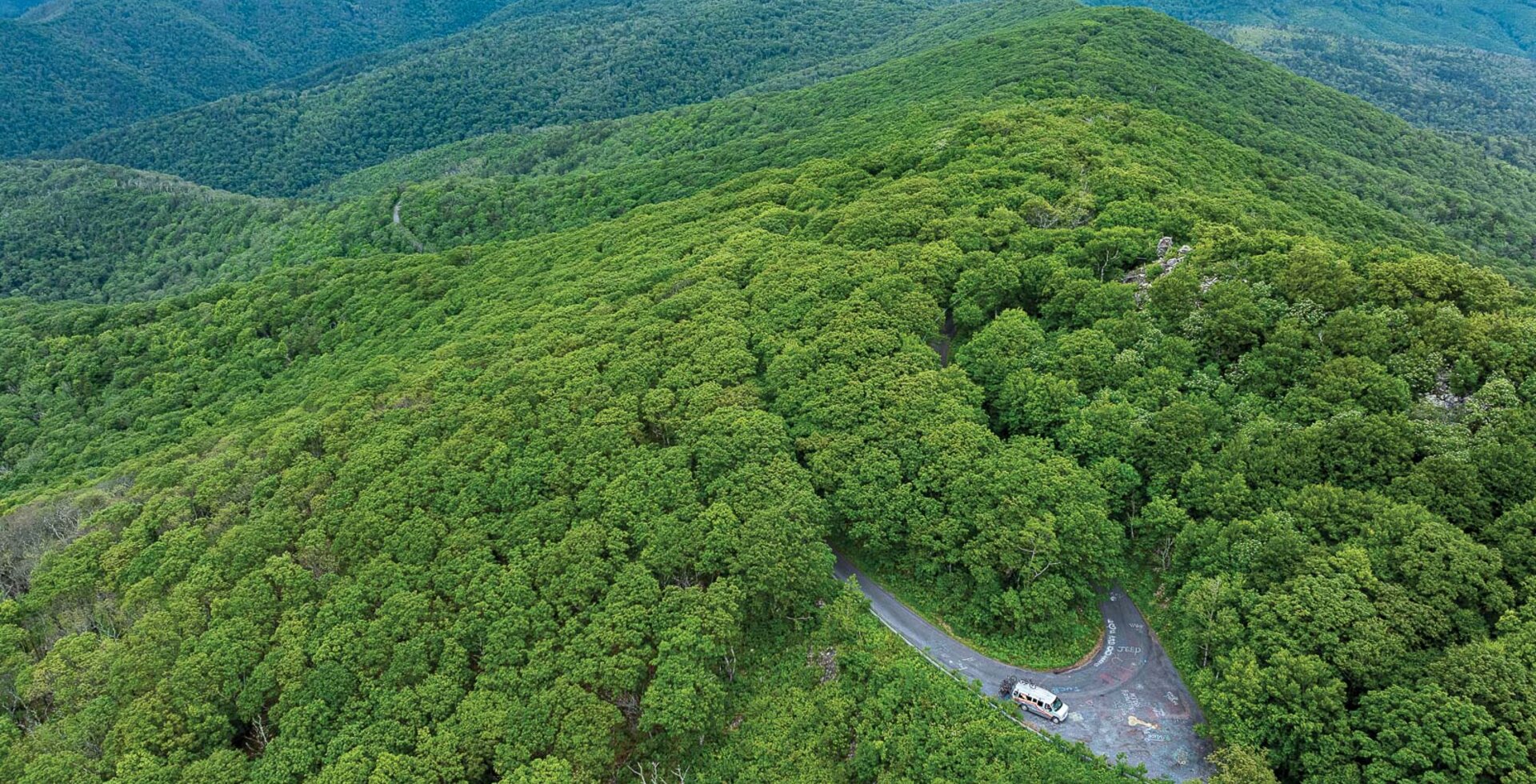 The Take Aim Cycling shuttle van is visible in an open spot in the otherwise dense canopy of the George Washington and Jefferson National Forest. The top of Reddish Knob, where a group of mountain bikers new to backcountry riding would start their journey, is nearby.