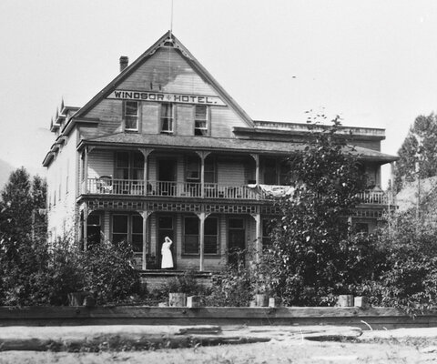 In a photograph taken from the banks of Lardeau Creek in the early 20th century, the Windsor Hotel is visible, along with a woman standing near its front door. The woman is likely the hotel’s proprietor Alice Jowett. Photo: Courtesy of Arrow Lakes Historical Society